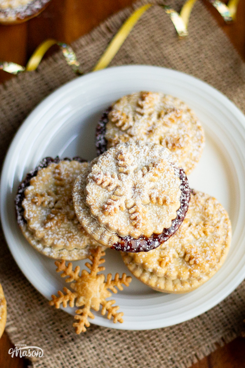 A stack of mince pies on a plate with shortcrust pastry snowflakes to the side.