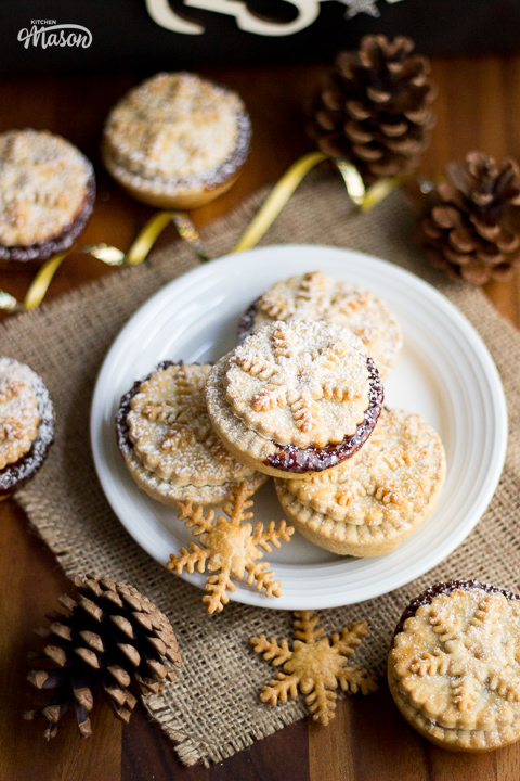 Pine cones and gold ribbon surrounding a white plate filled with mince pies.