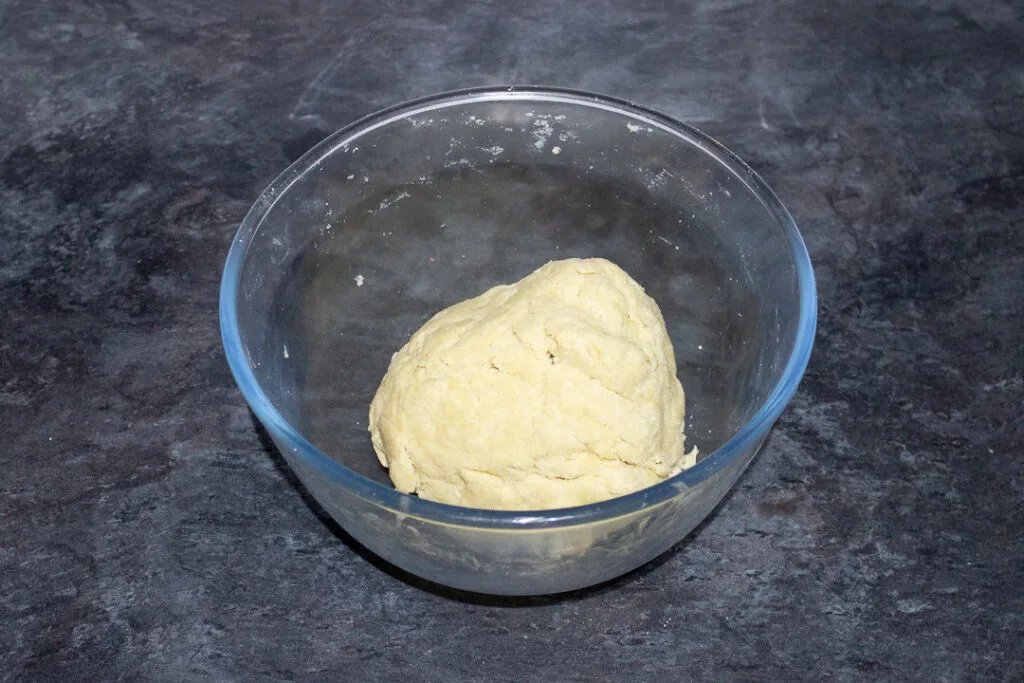 A ball of shortcrust pastry in a glass mixing bowl.