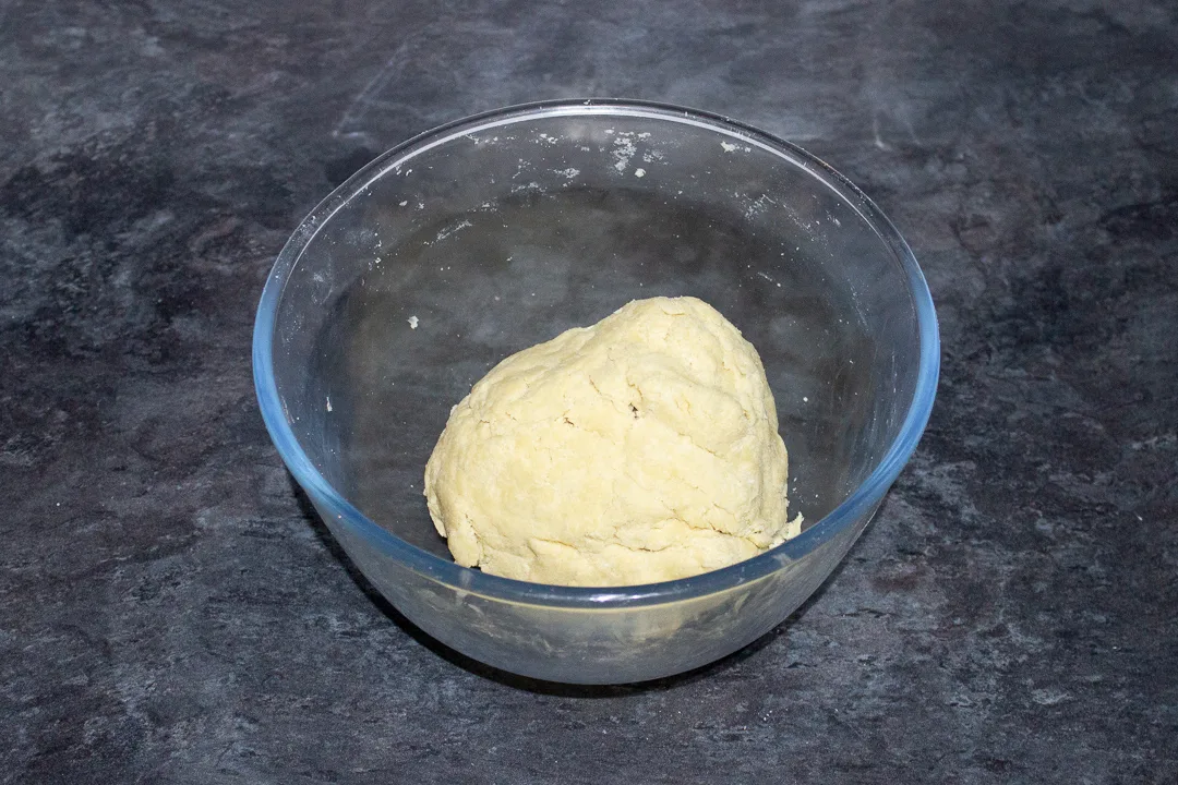 A ball of shortcrust pastry in a glass mixing bowl.