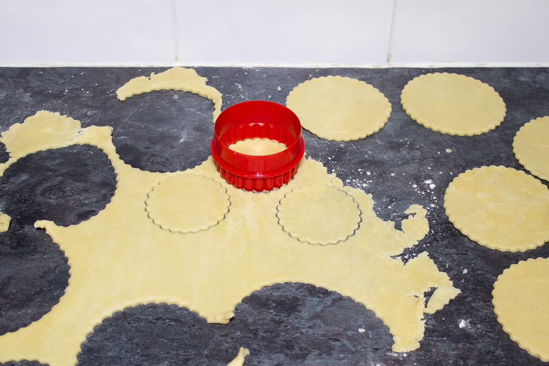 Rolled out shortcrust pastry being cut into fluted rounds.