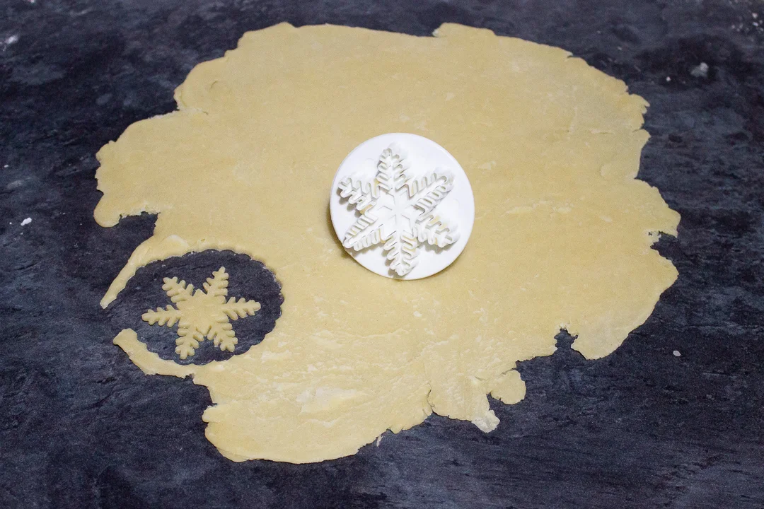 Shortcrust pastry snowflakes being cut out using a snowflake plunge cutter.