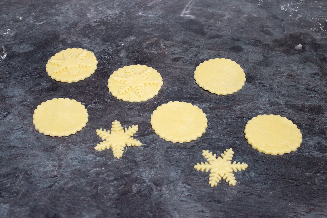 Shortcrust pastry snowflakes being stuck to mince pie lids.