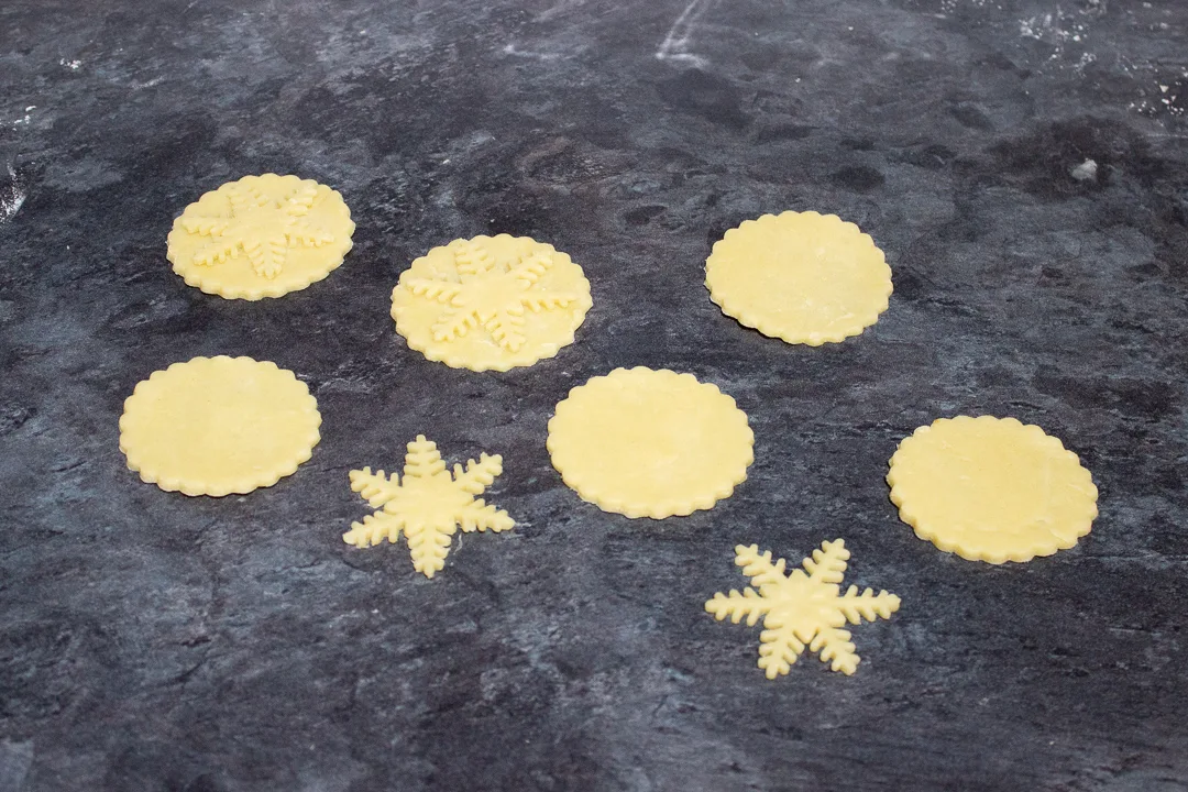 Shortcrust pastry snowflakes being stuck to mince pie lids.
