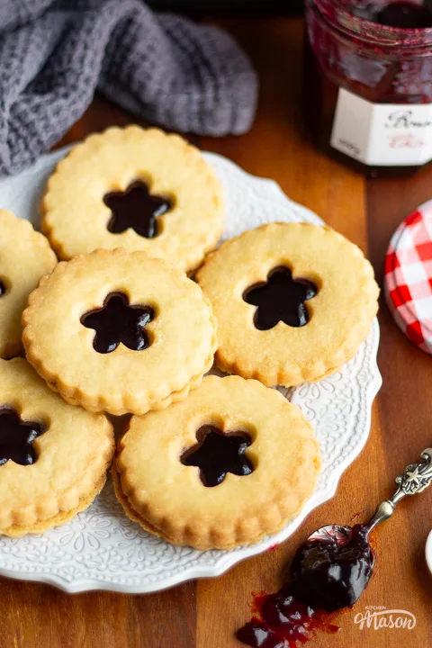 A plate filled with homemade hammy dodgers with a spoon of black cherry jam to the side.