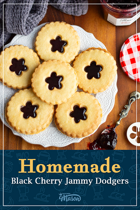 A white decorative plate of 6 homemade jammy dodgers with a spoon filled with jam to the side. A text overlay says "Homemade black cherry jammy dodgers".
