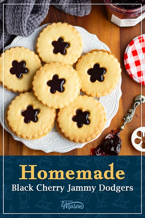 A white decorative plate of 6 homemade jammy dodgers with a spoon filled with jam to the side. A text overlay says "Homemade black cherry jammy dodgers".