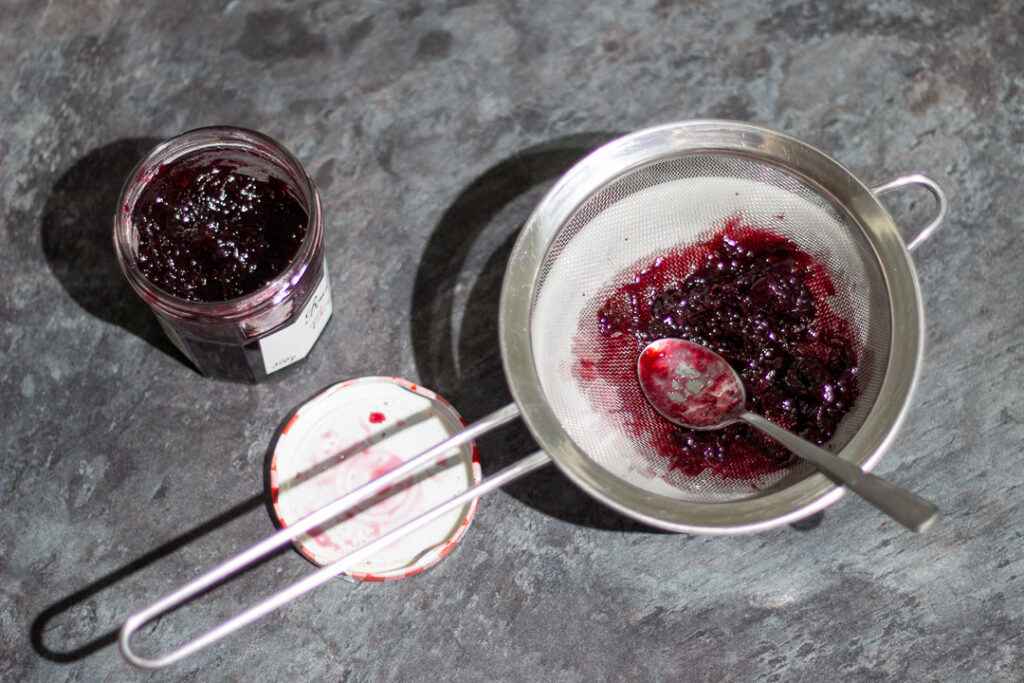 Black cherry jam being pushed through a sieve.