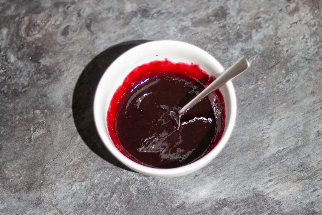 Sieved black cherry jam in a small bowl with a spoon.