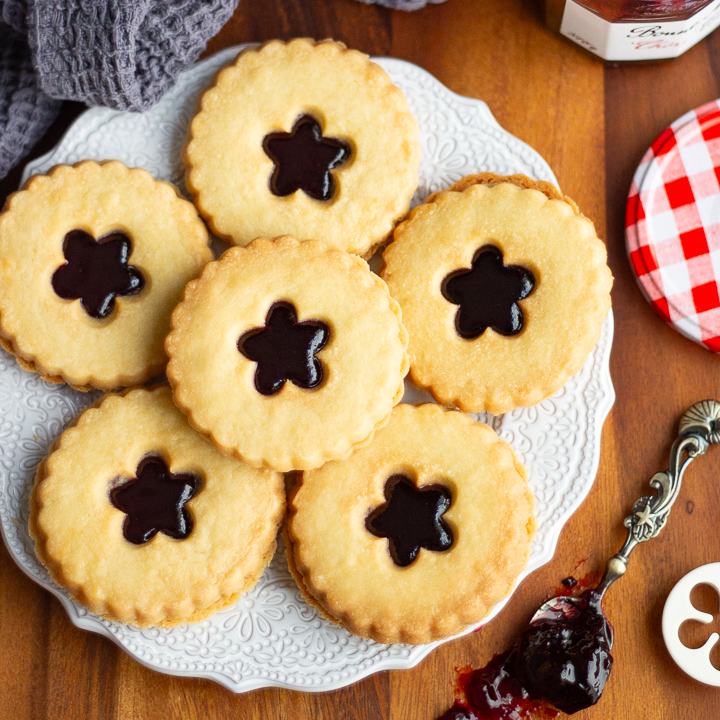 Lots of black cherry jammy dodgers on a patterned white plate.