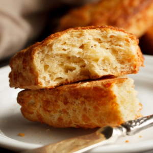 A cheese scone split in half with a knife on a plate.