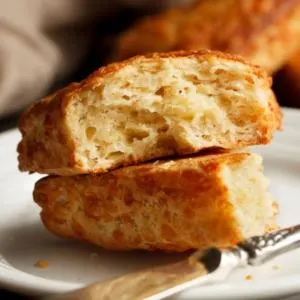 A cheese scone split in half with a knife on a plate.