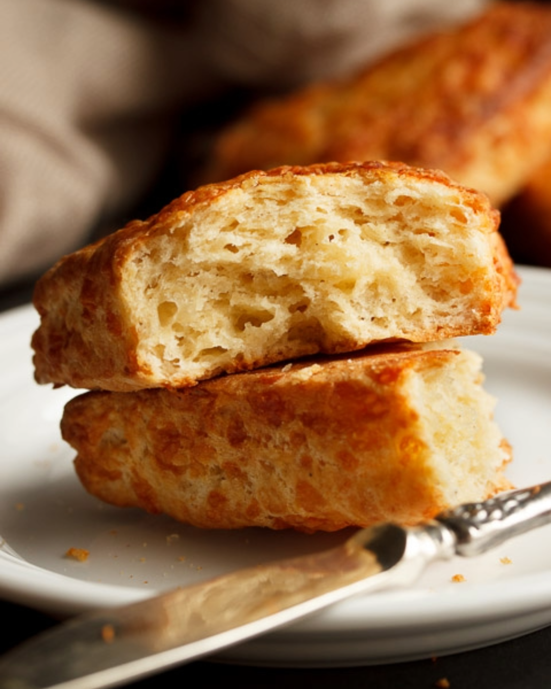 A cheese scone split in half with a knife on a plate.