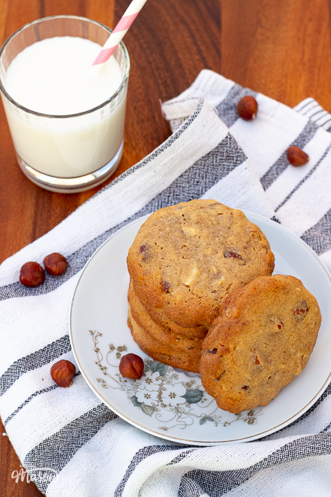 A glass of milk with a straw next to a plate of several nut biscuits.