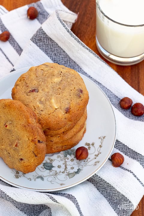 A grey and white striped tea towel topped with a plate of nut biscuits and a glass of milk.