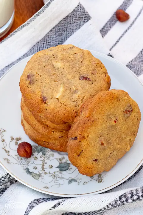 A small stack of nut biscuits on a little flower patterned plate, set on a tea towel.