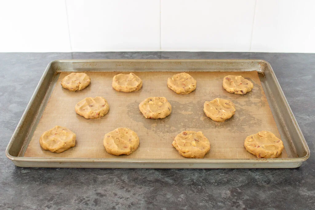 Unbaked nut biscuits flattened slightly on a large lined baking tray.