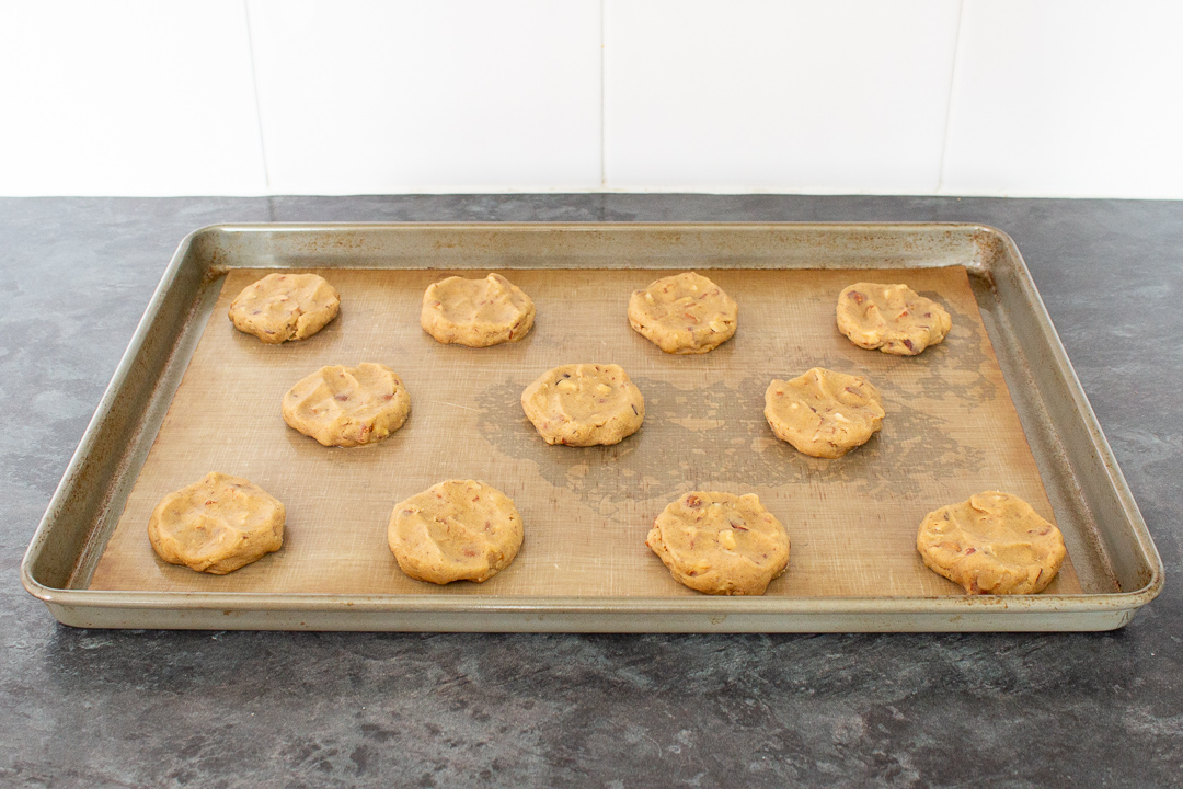 Unbaked nut biscuits flattened slightly on a large lined baking tray.
