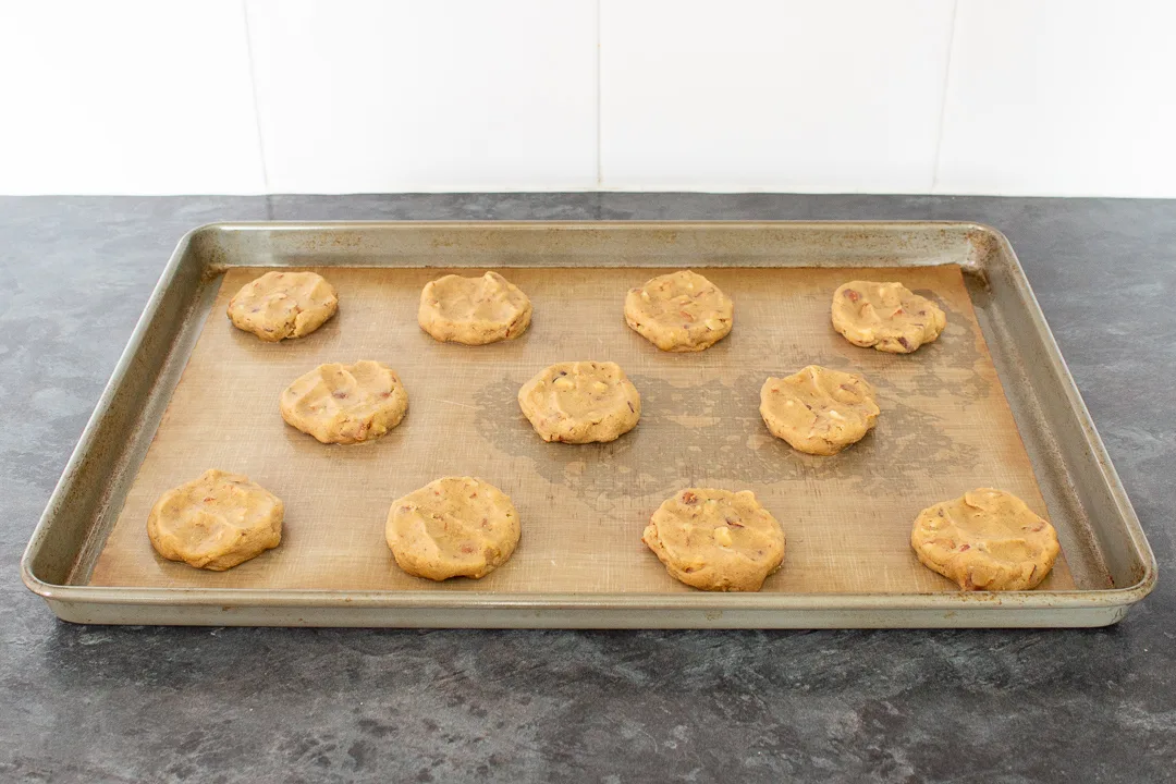 Unbaked nut biscuits flattened slightly on a large lined baking tray.