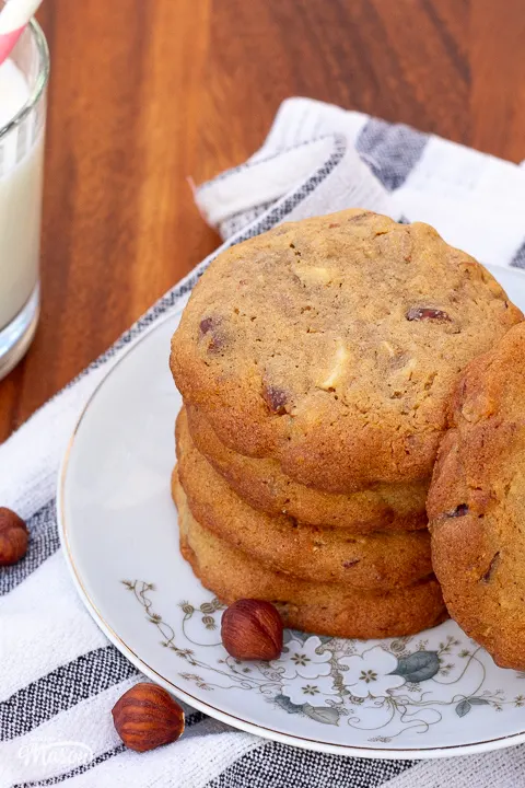 Several nut biscuits stacked on a plate, with whole hazelnuts scattered around it.