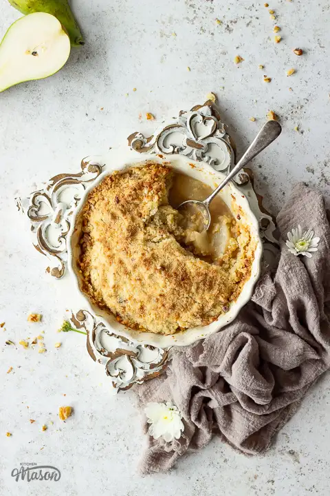 A dish filled with pear crumble on a wooden board. The crumble topping is crisp and golden, and the filling is juicy and shiny.