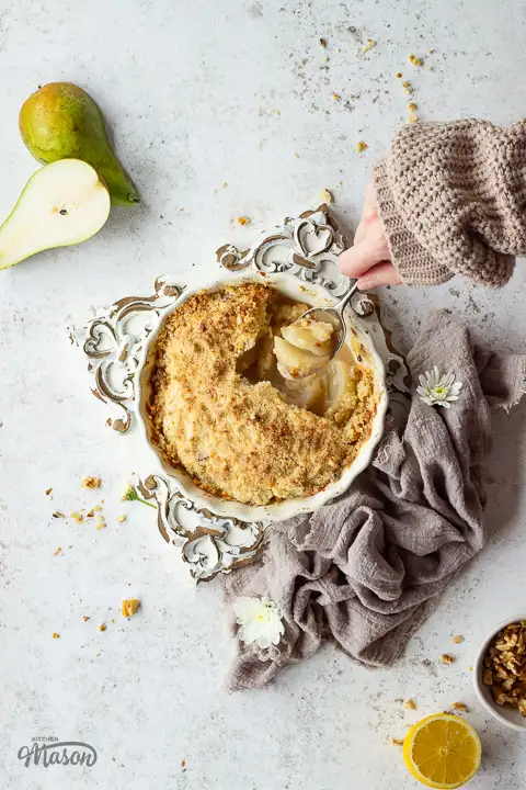 Someone spooning pear crumble from a baking dish.