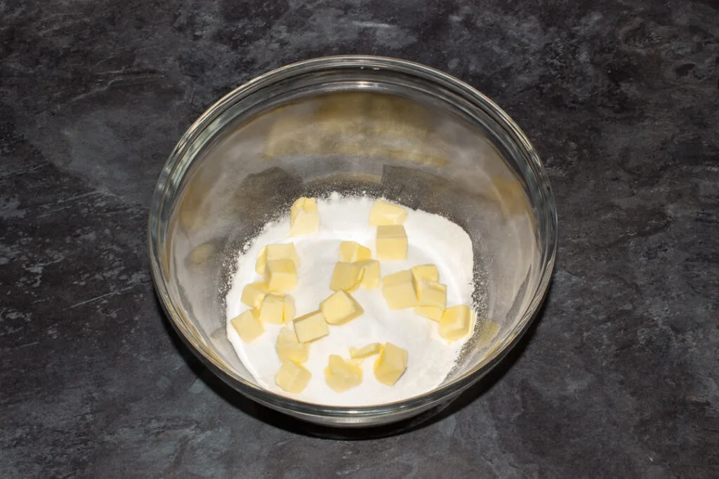 A mixing bowl containing flour, sugar, salt and cubed butter.