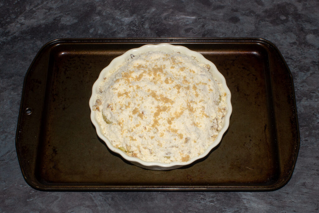 A unbaked pear crumble in a dish on a baking tray, ready for the oven.