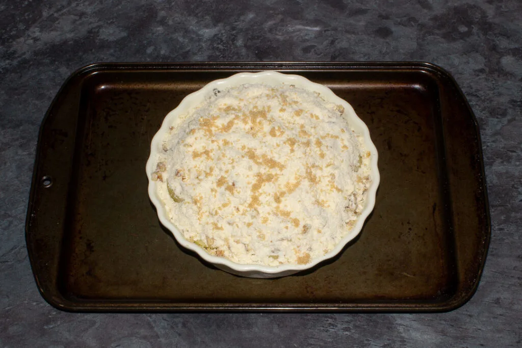 A unbaked pear crumble in a dish on a baking tray, ready for the oven.