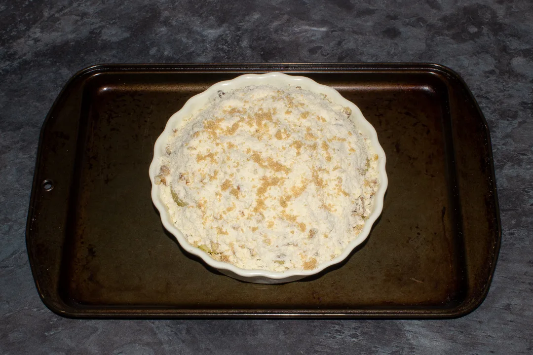 A unbaked pear crumble in a dish on a baking tray, ready for the oven.