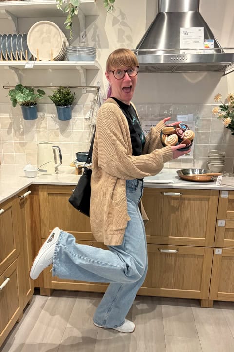A very cheerful Emma in an IKEA showroom kitchen holding a plate of play cinnamon buns.