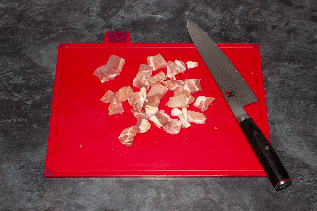 Chopped bacon on a chopping board with a knife.