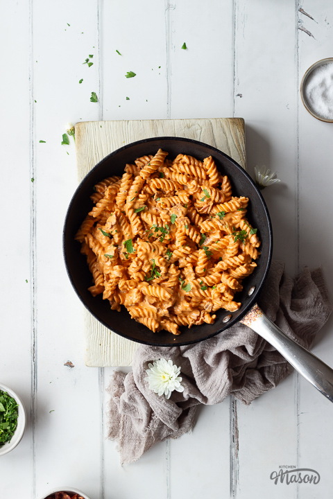 Creamy bacon pasta in a frying pan on a wooden chopping board.