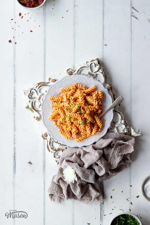 A large plate filled with creamy bacon pasta on an embossed wooden board.