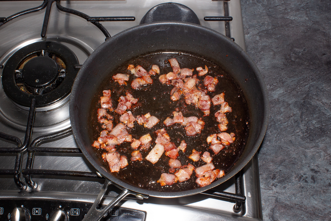 Bacon pieces frying in a large frying pan.