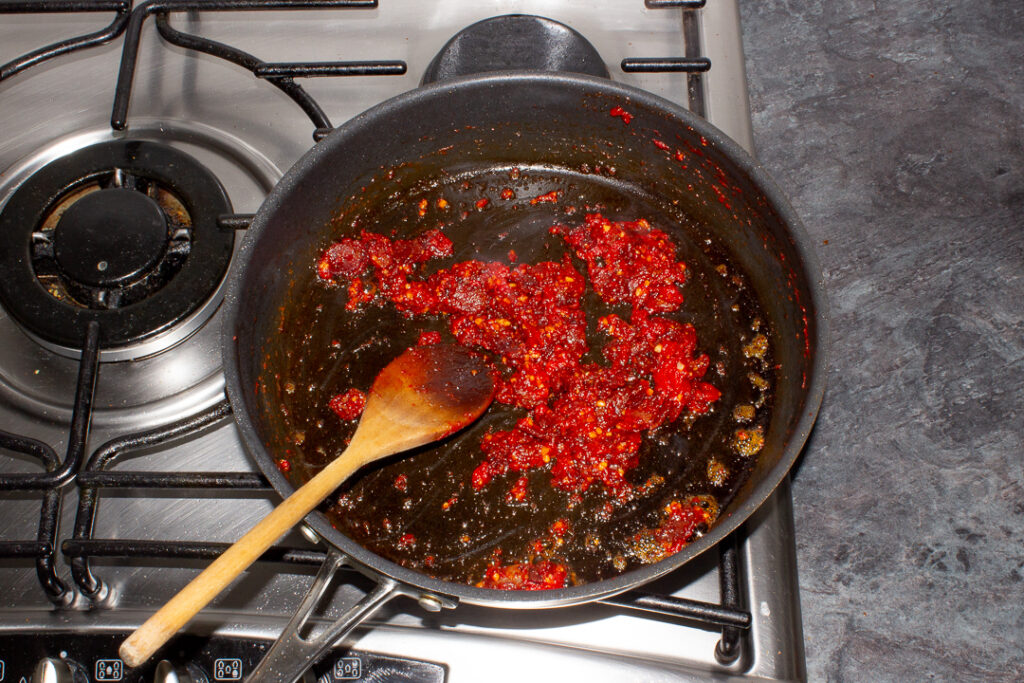 Bacon, garlic and tomato puree frying in a pan with a wooden spoon.