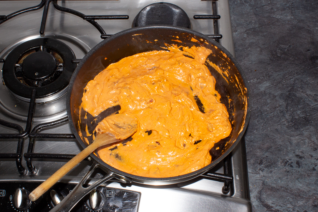 Mascarpone added to a frying pan with bacon, garlic and tomato puree to make a sauce.