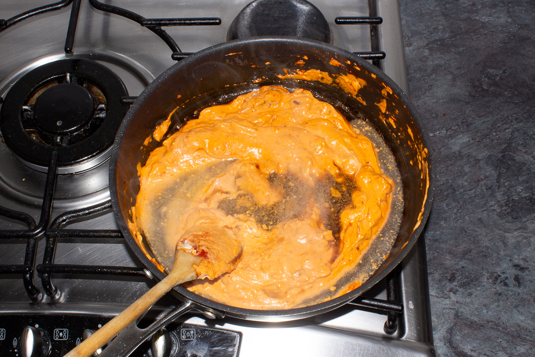 Pasta cooking water being stirred through a pasta sauce in a frying pan.