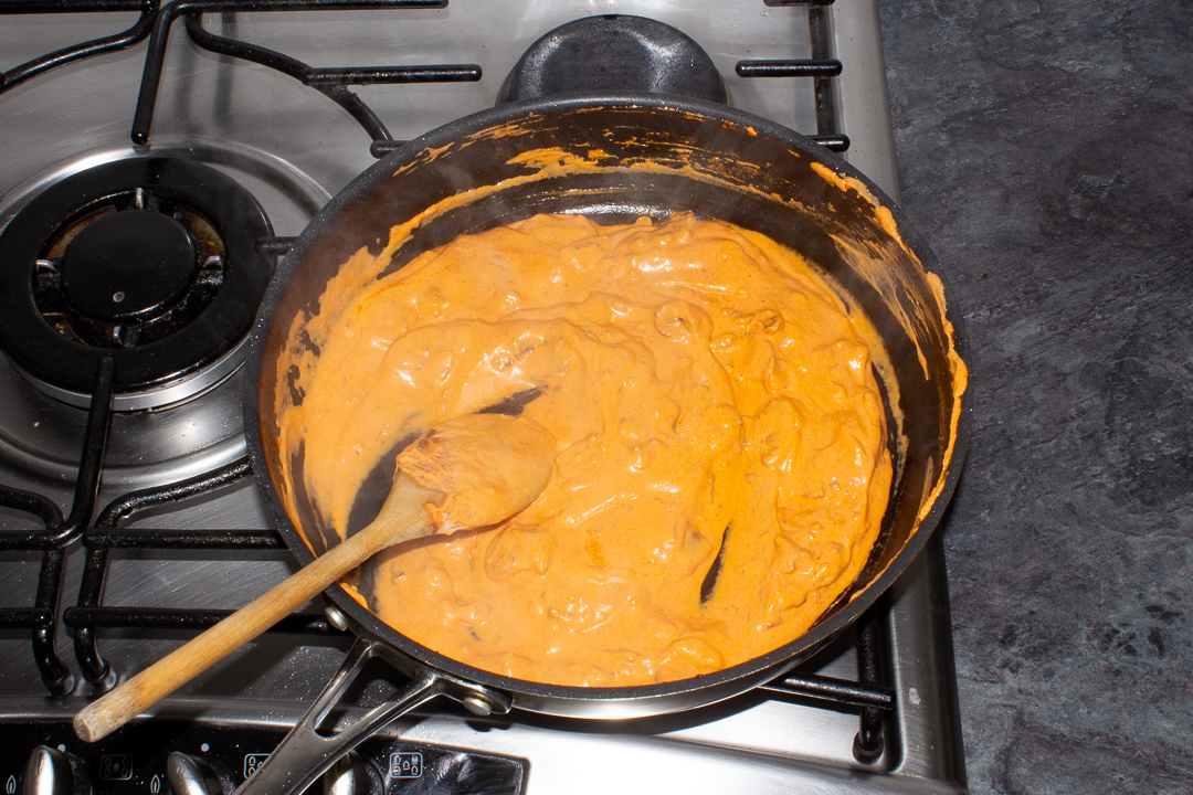 Creamy bacon pasta sauce in a frying pan with a wooden spoon.