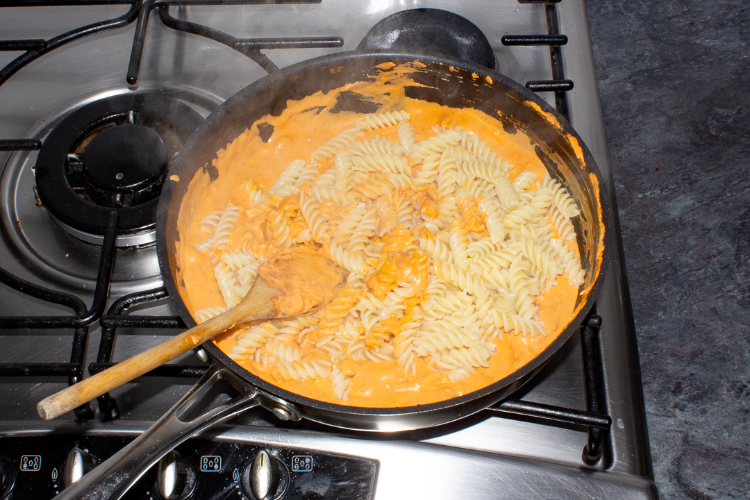 Fusilli pasta being stirred through a creamy bacon sauce.