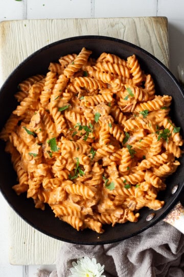 A large frying pan filled with creamy bacon pasta sat on a wooden board.