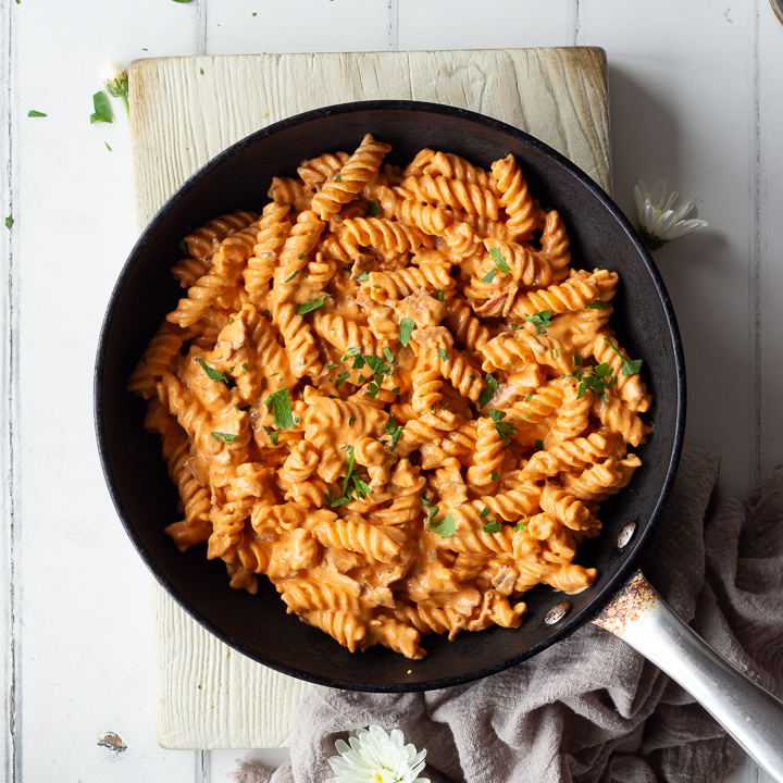 A large frying pan filled with creamy bacon pasta sat on a wooden board.