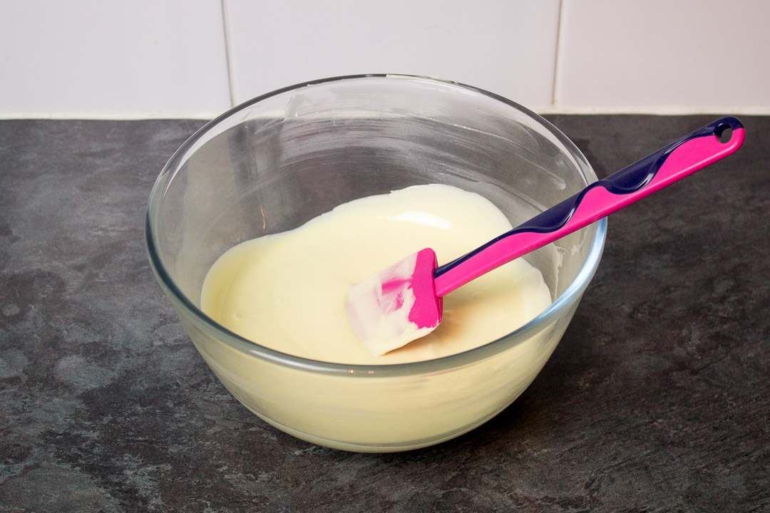 Melted white chocolate in a mixing bowl with a spatula.