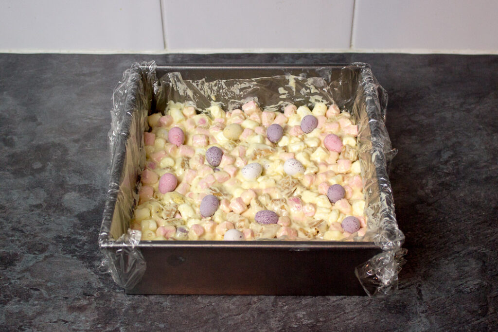 Mini Eggs pressed into the top of a white chocolate rocky road mixture in a lined square baking tin.