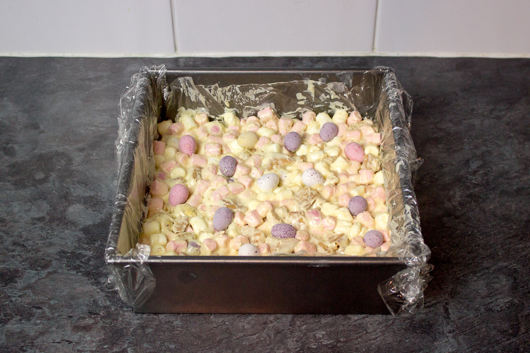 Mini Eggs pressed into the top of a white chocolate rocky road mixture in a lined square baking tin.