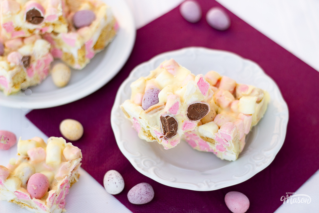 Several squares of Mini Egg rocky road spread over two decorative white plates and a purple napkin.
