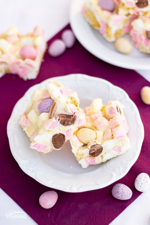 A decorative white plate of Mini Egg rocky road bars set over a purple napkin.