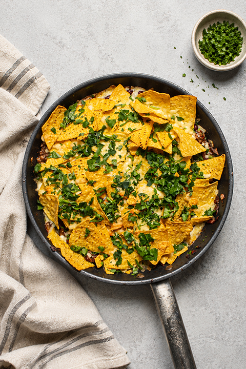 A pan filled with a beef and kidney bean mixture, topped with lots of melted cheese and nachos.