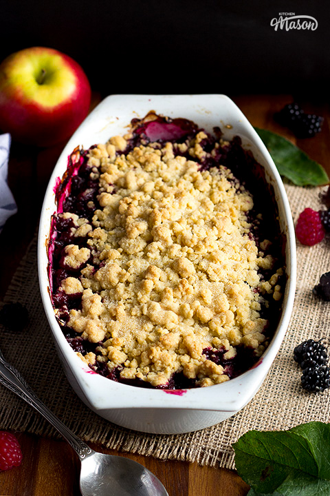 An apple and berry crumble in a decorative dish on hessian fabric.