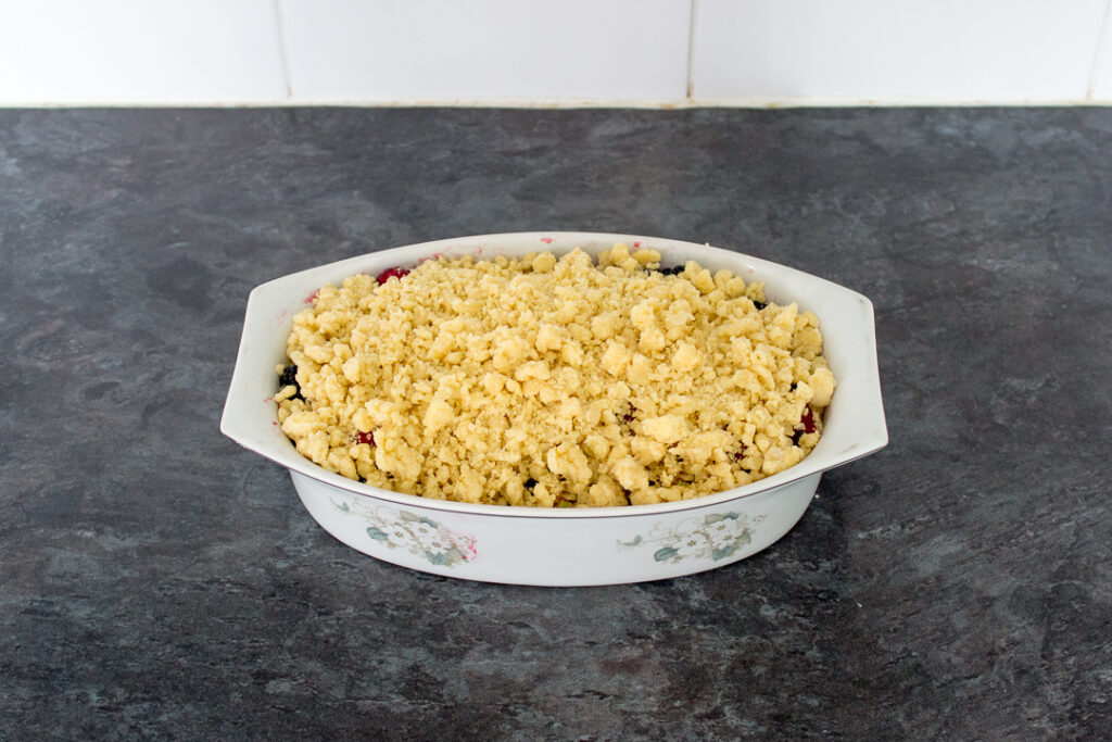 Summer fruits topped with homemade crumble mixture in a decorative dish.